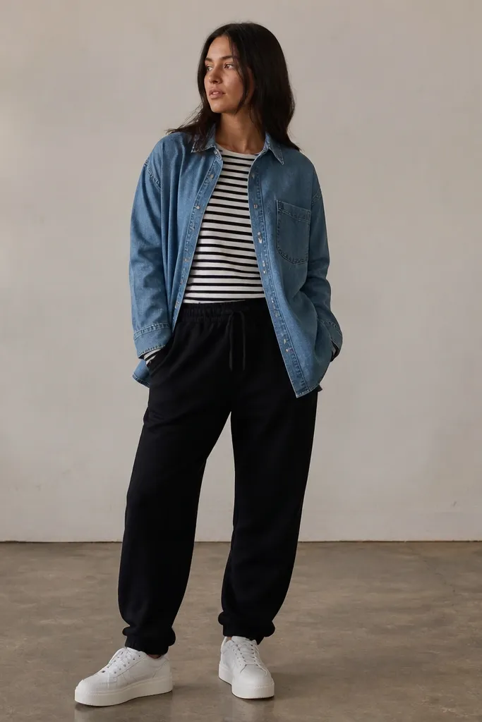 Black sweatpants with a black-and-white striped long-sleeve tee. Over it is a medium-wash denim overshirt. The shoes are white sneakers with a slightly thicker sole.