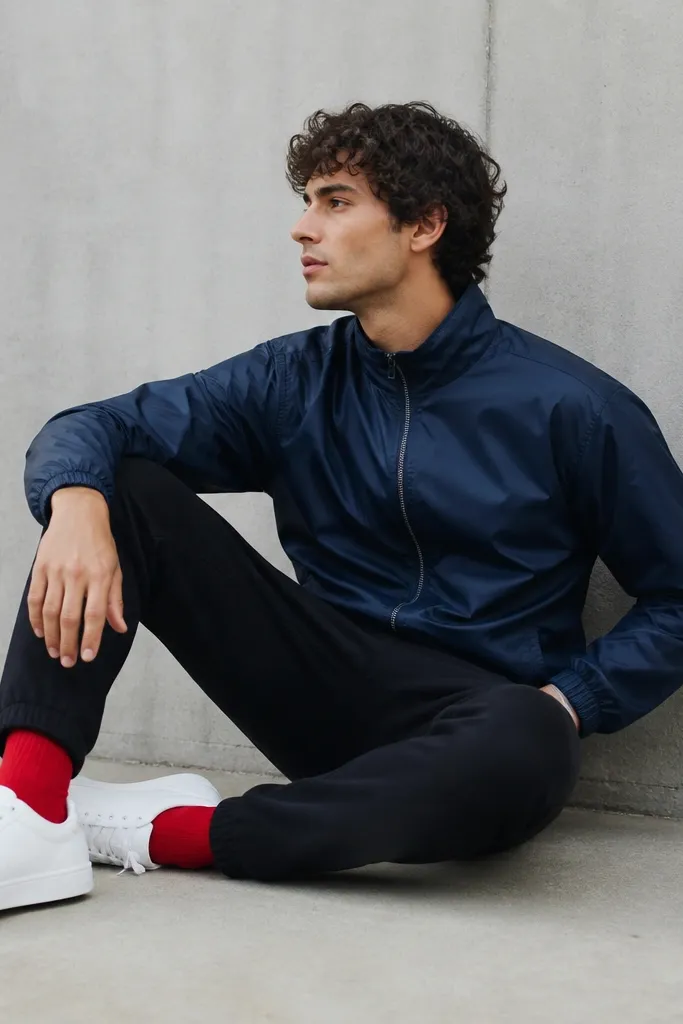 Black sweatpants with a navy windbreaker jacket. The jacket has a subtle sheen and a zipper. The sneakers are white, and the socks are a bright red that shows above the shoe.