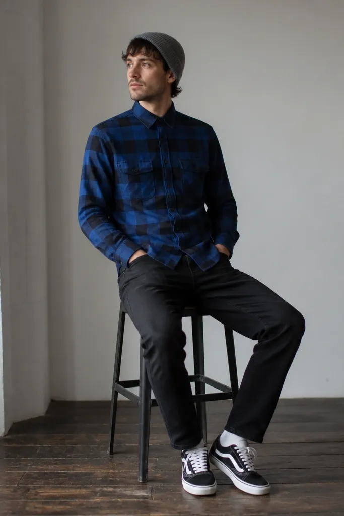A cobalt blue check flannel worn buttoned, paired with black jeans. A gray beanie and black-and-white sneakers appear.
