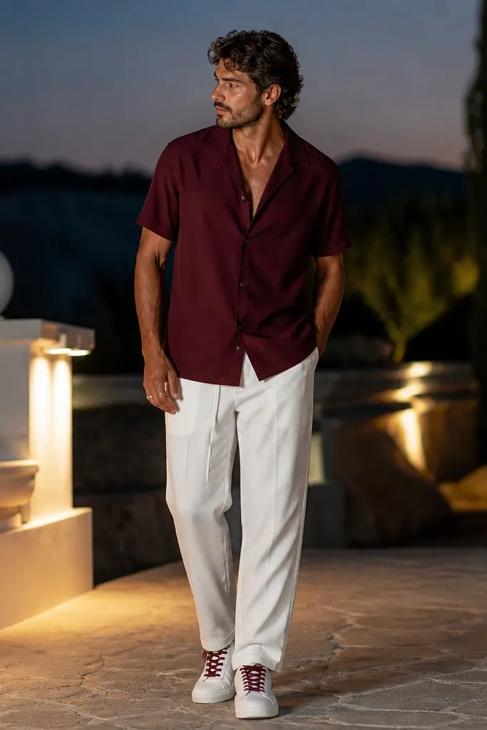 White track pants with a burgundy camp collar shirt, slightly open at the top. White sneakers with burgundy laces and a gold ring. Evening outdoor setting.
